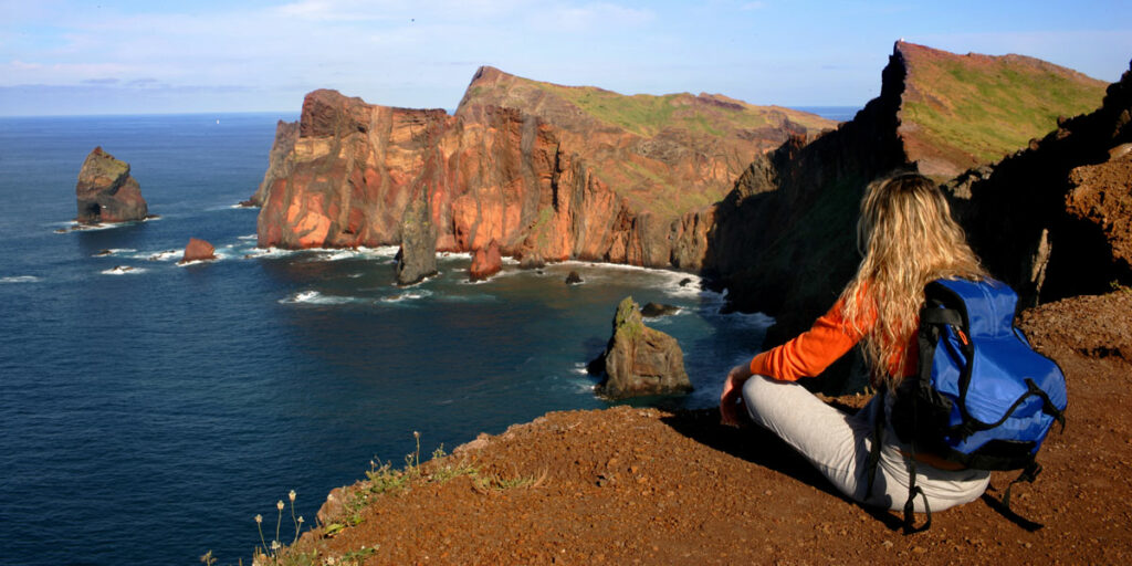 Woman sitting with back to the camera looking at the ocean and cliffs in Madeira