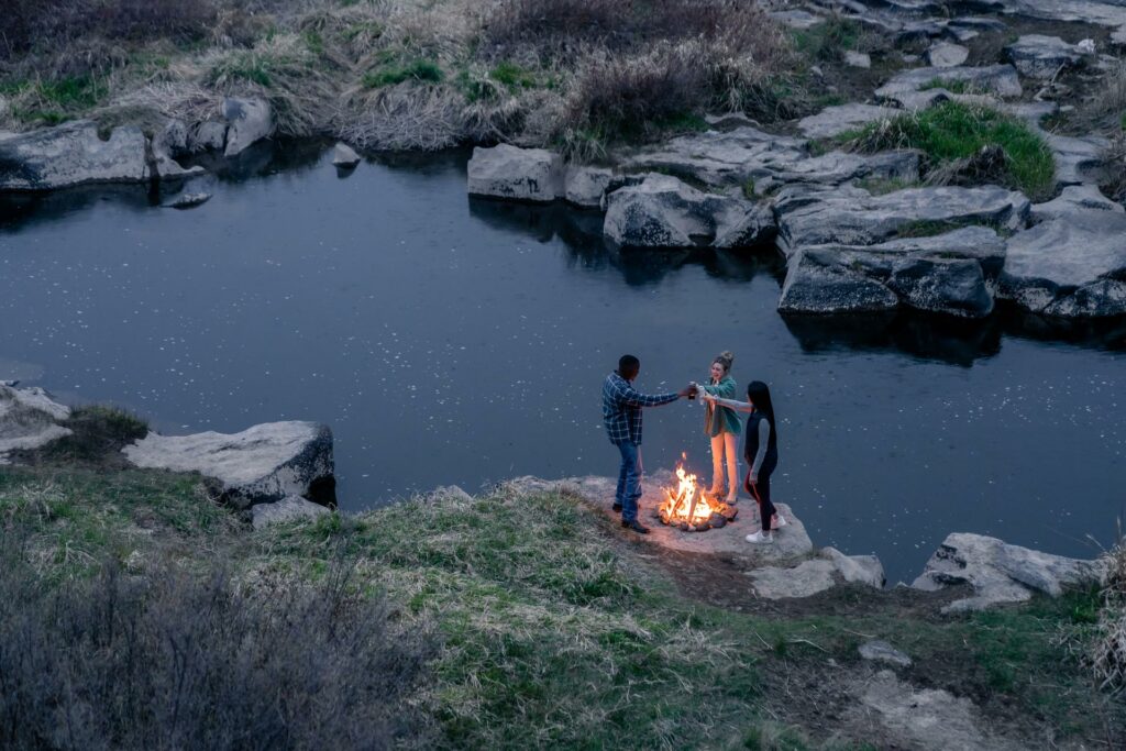 Group of people drinking around a fire by a river