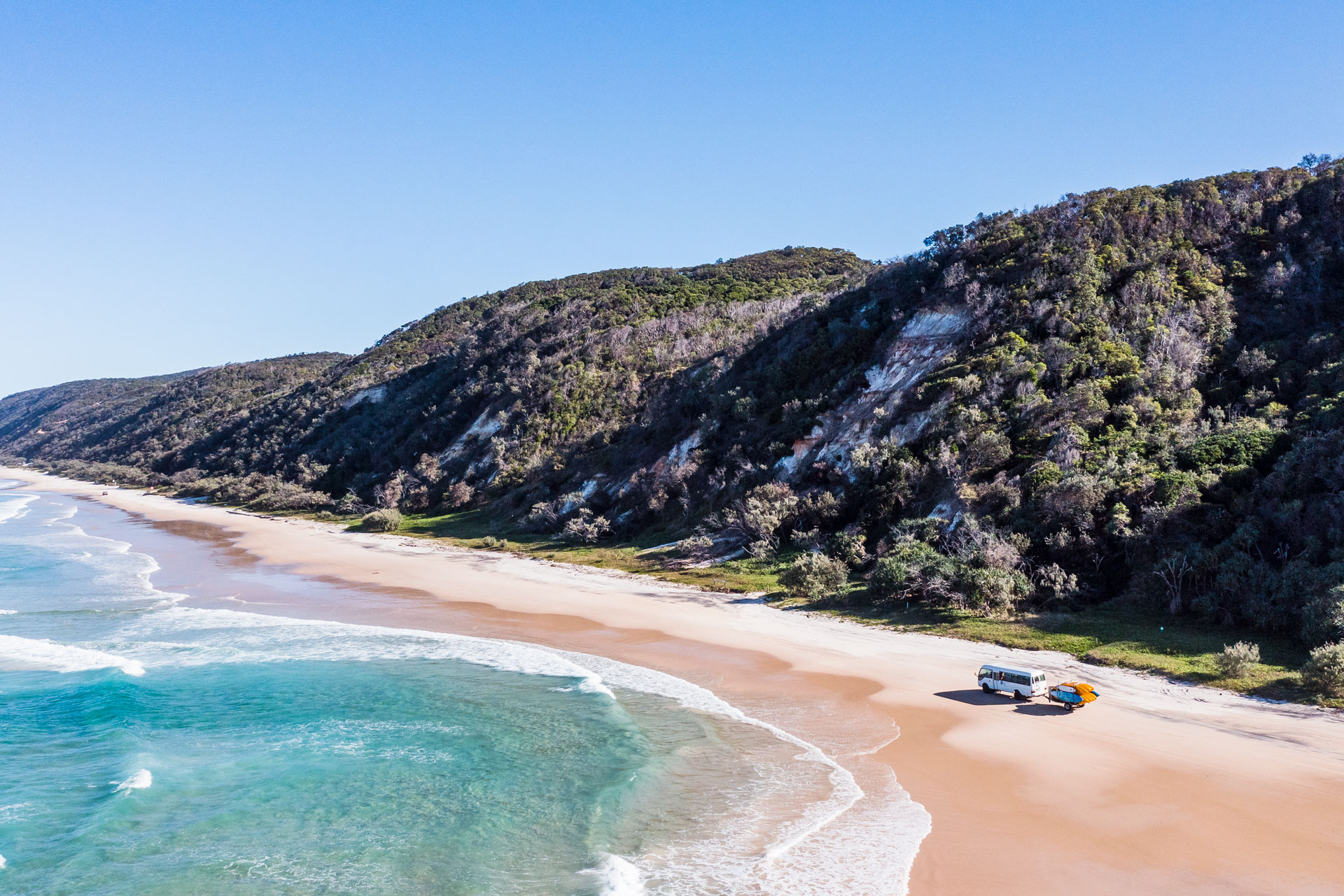 Noosa beach with mountains in the background and a car driving on the sand