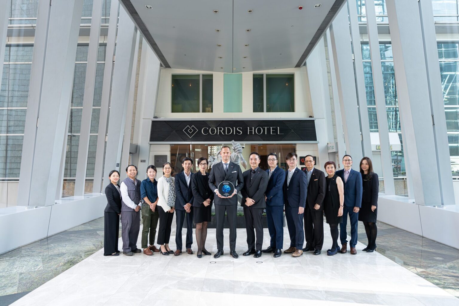 Cordis, Hong Kong staff in work wear smiling at the camera with an EarthCheck master plaque