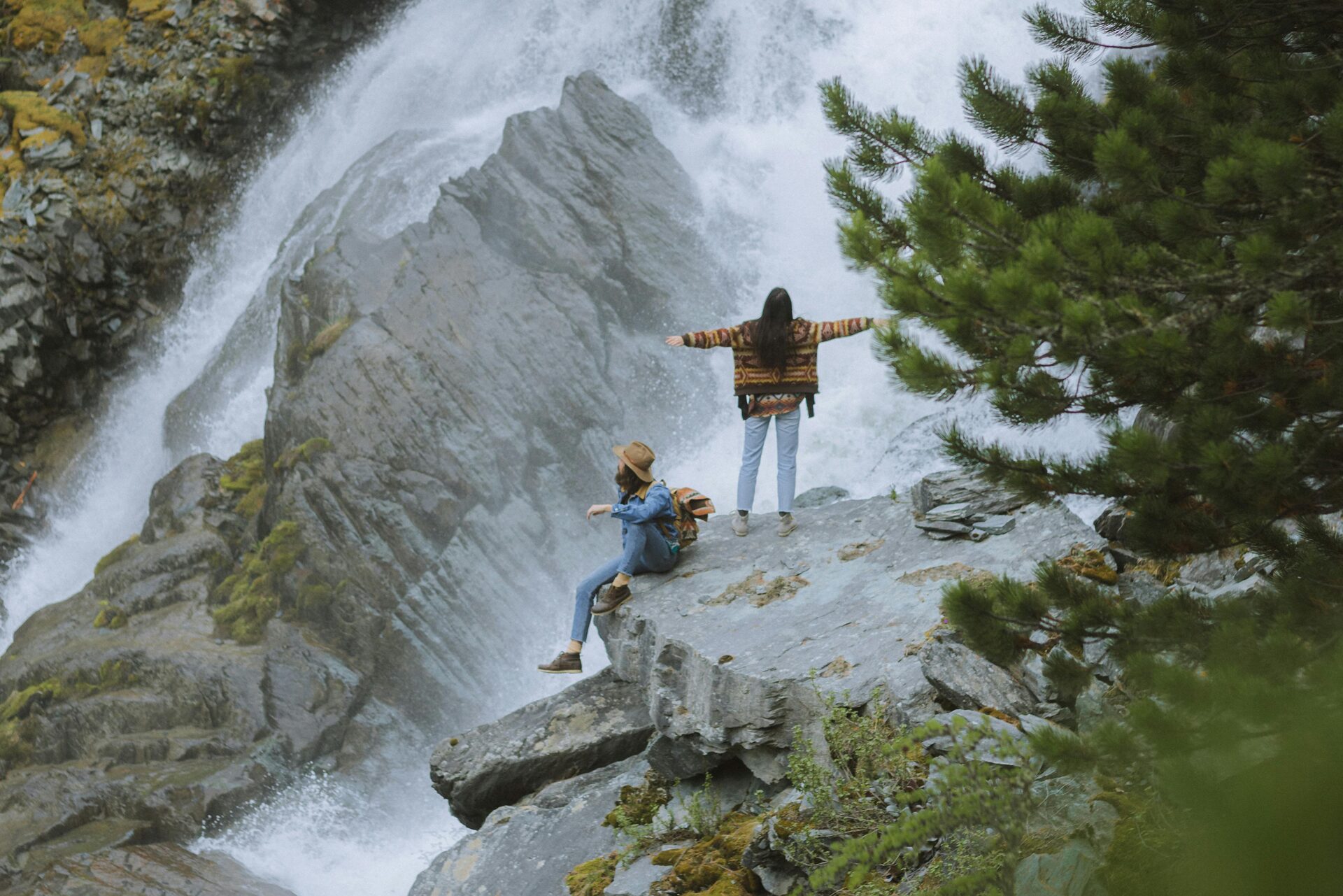 Two travellers standing on a rock looking at a waterfall