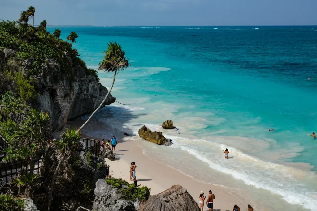 Aerial photo of a beach in Riviera Maya. Some people can be seen on the beach and swimming in the water.