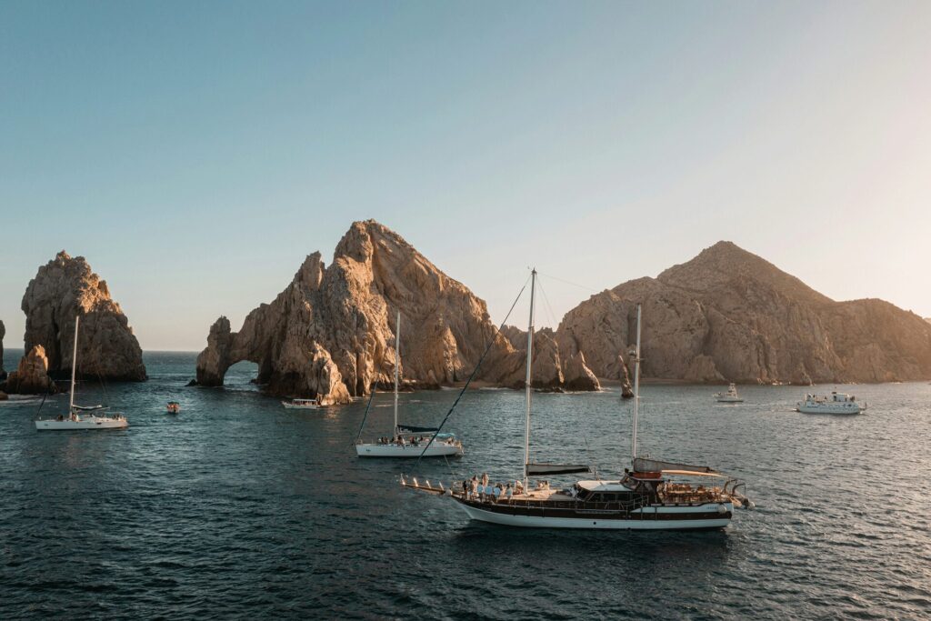 Several boats in the ocean with rock formations coming out of the water in the background