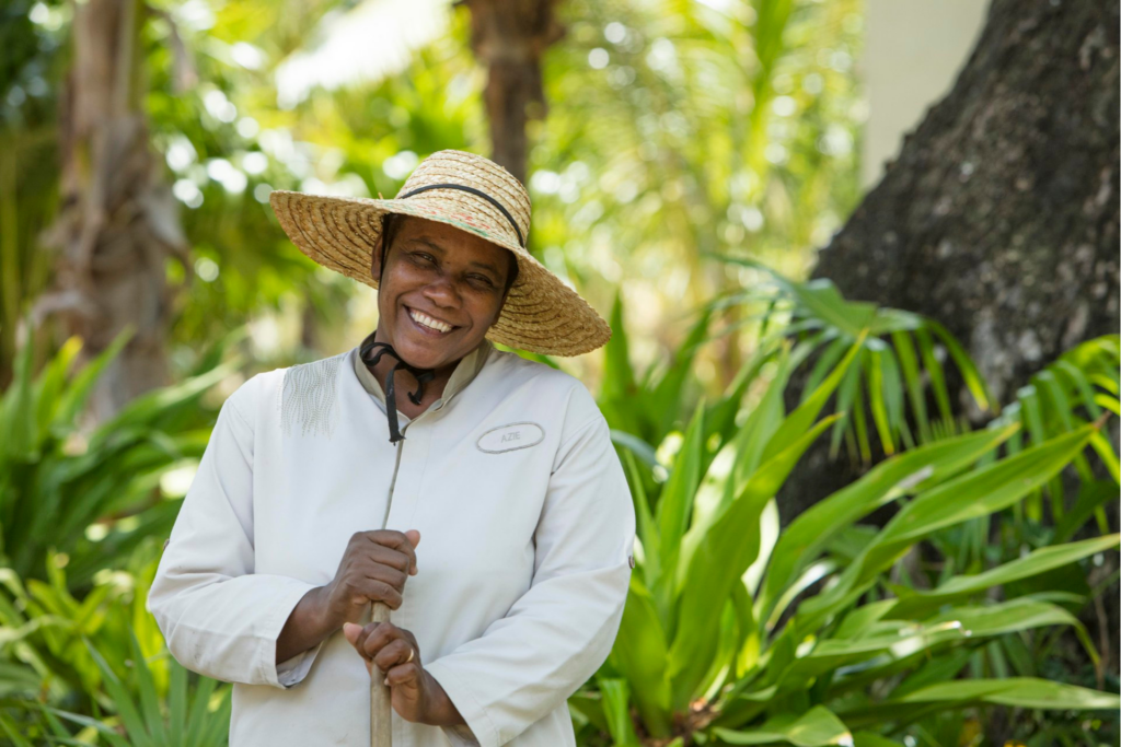 Beachcomber staff member pictured outside against a backdrop of plants, smiling at the camera and wearing a wide brim straw hat