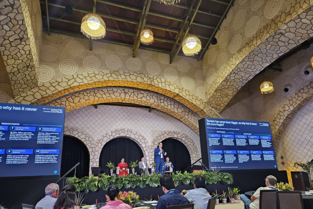 Four people on stage in a panel presentation, with presentation slides on either sides of them